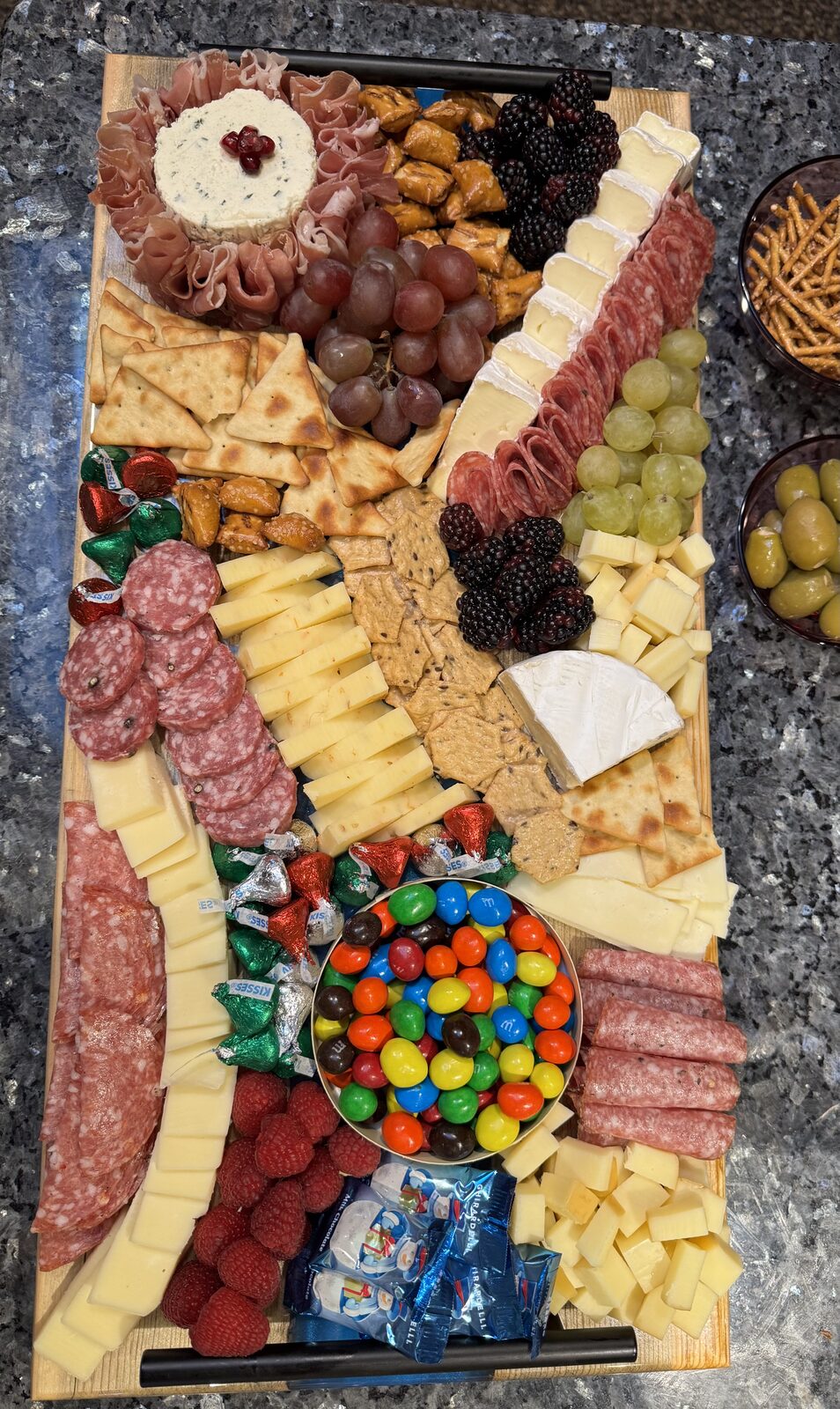 Holiday board with prosciutto, cheese ball, brie, raspberries, chocolates and candies