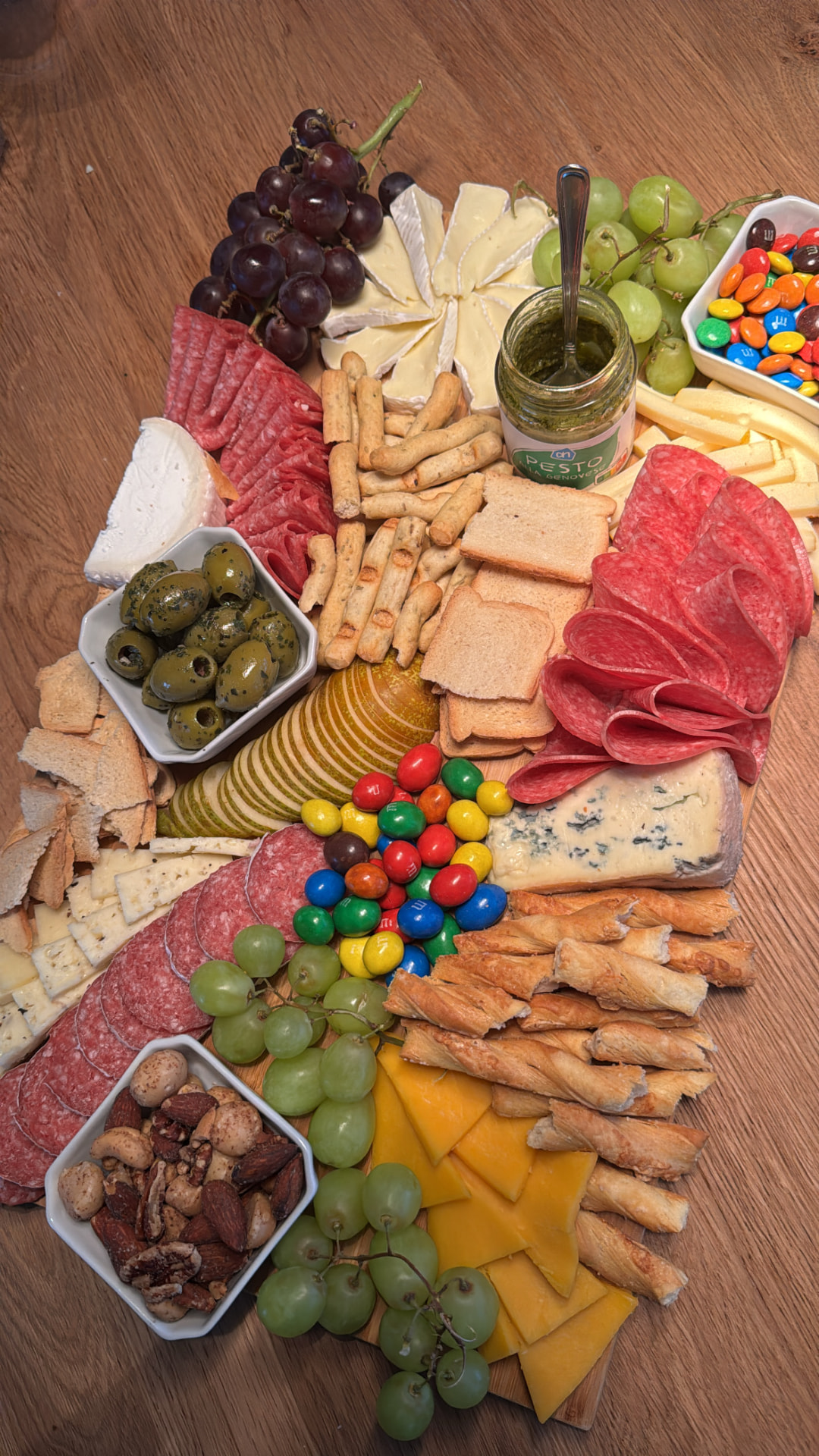 Rustic wooden table spread with salami, brie, blue cheese, breadsticks, olives, grapes and candies