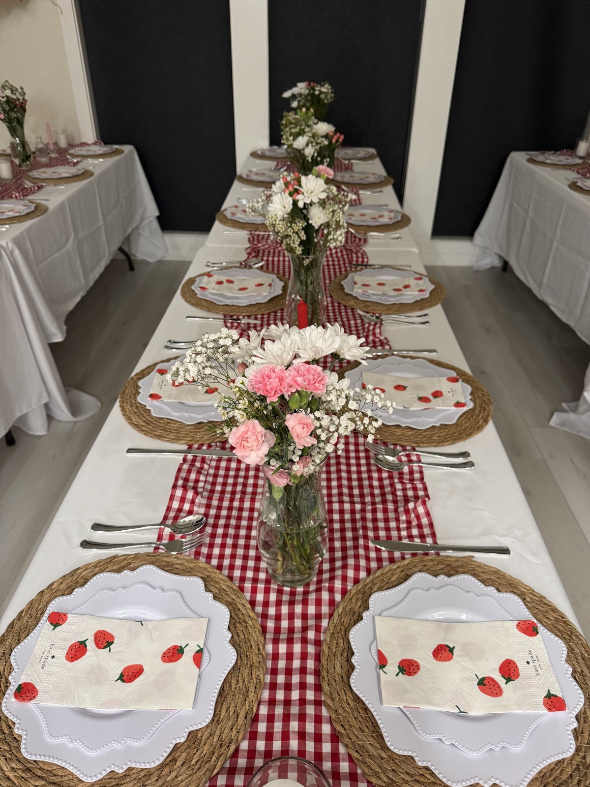 The long guest table set with gingham runners, strawberry napkins and flowers