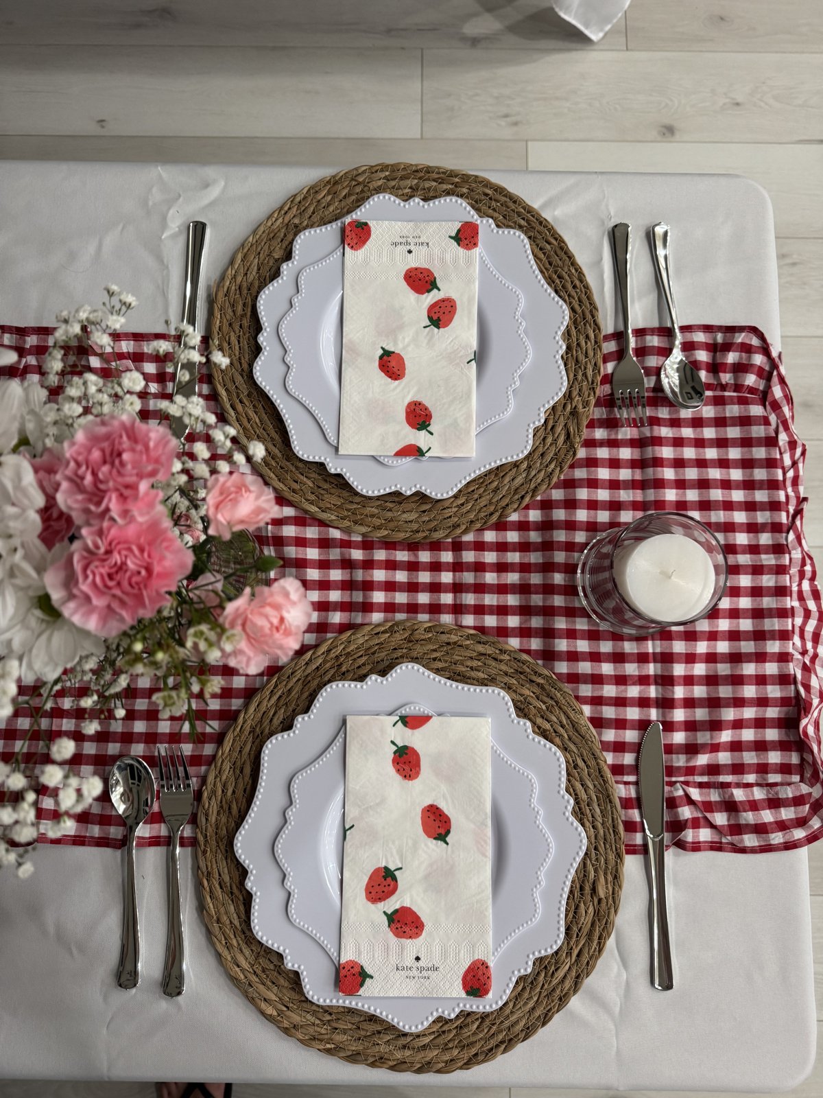 Close-up of a place setting with scalloped plates and strawberry napkins