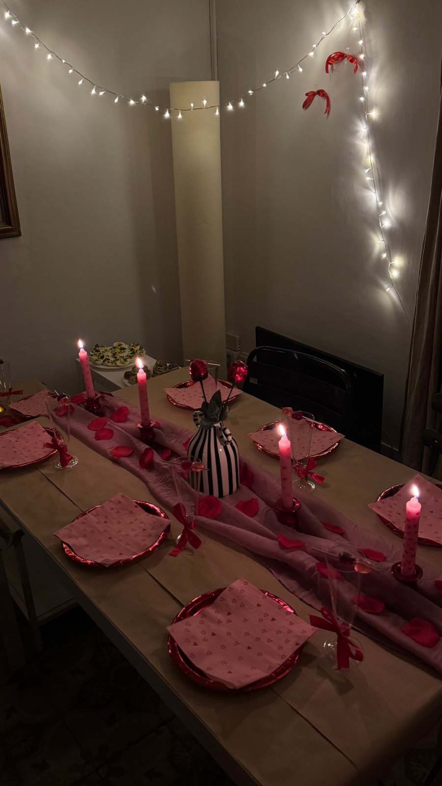 The Galentine's Day table — pink and red place settings, heart candles and rose petals under fairy lights