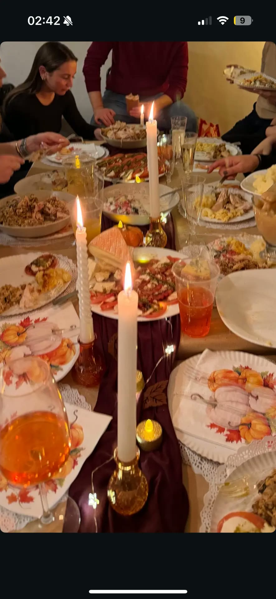 The Thanksgiving dinner table seen down its length — candles, autumn plates and food shared among friends